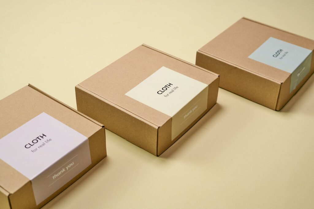 pexels-photo-9594428-9594428-5 Three minimalist cardboard packages labeled 'CLOTH' on a yellow background.